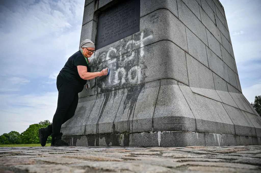 A member of the public cleans the Robert the Bruce Statue which has been defaced with graffiti saying "Racist King" in Bannockburn, Scotland, on June 12, 2020. (Jeff J. Mitchell/Getty Images)