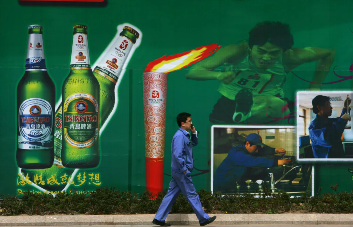 A worker walks past a billboard featuring beer and Olympic Torch at the Tsingtao Beer Factory, China's biggest beer brewery and the Official Domestic Beer Sponsor of the Beijing 2008 Olympic Games in Qingdao of Shandong Province, China, on April 25, 2008. (China Photos/Getty Images)