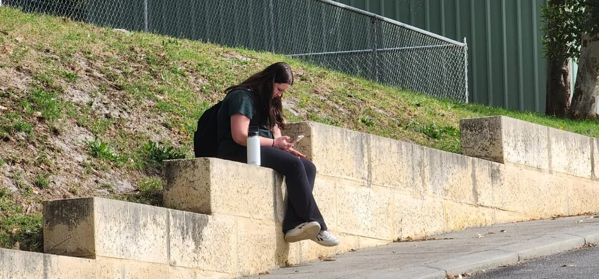 A high school student looks at her phone while waiting to be picked up in Albany, Western Australia, on Oct. 17, 2023. (Susan Mortimer/The Epoch Times)