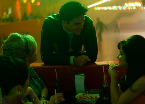 man leans on booth talking to girls in PRISCILLA