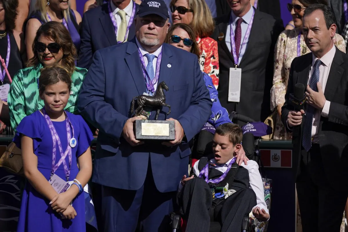 Cody Dorman, center below right, sits alongside his father Kelly Dorman, left holding trophy, mother Leslie Dorman, second from left, behind, and sister Kylie, left, after jockey Junior Alvarado rode Cody's Wish to win the Breeders' Cup Dirt Mile horse race at Santa Anita Park in Arcadia, Calif., on Nov. 4, 2023. Cody's Wish is named after Cody Dorman. (Ashley Landis/AP Photo)