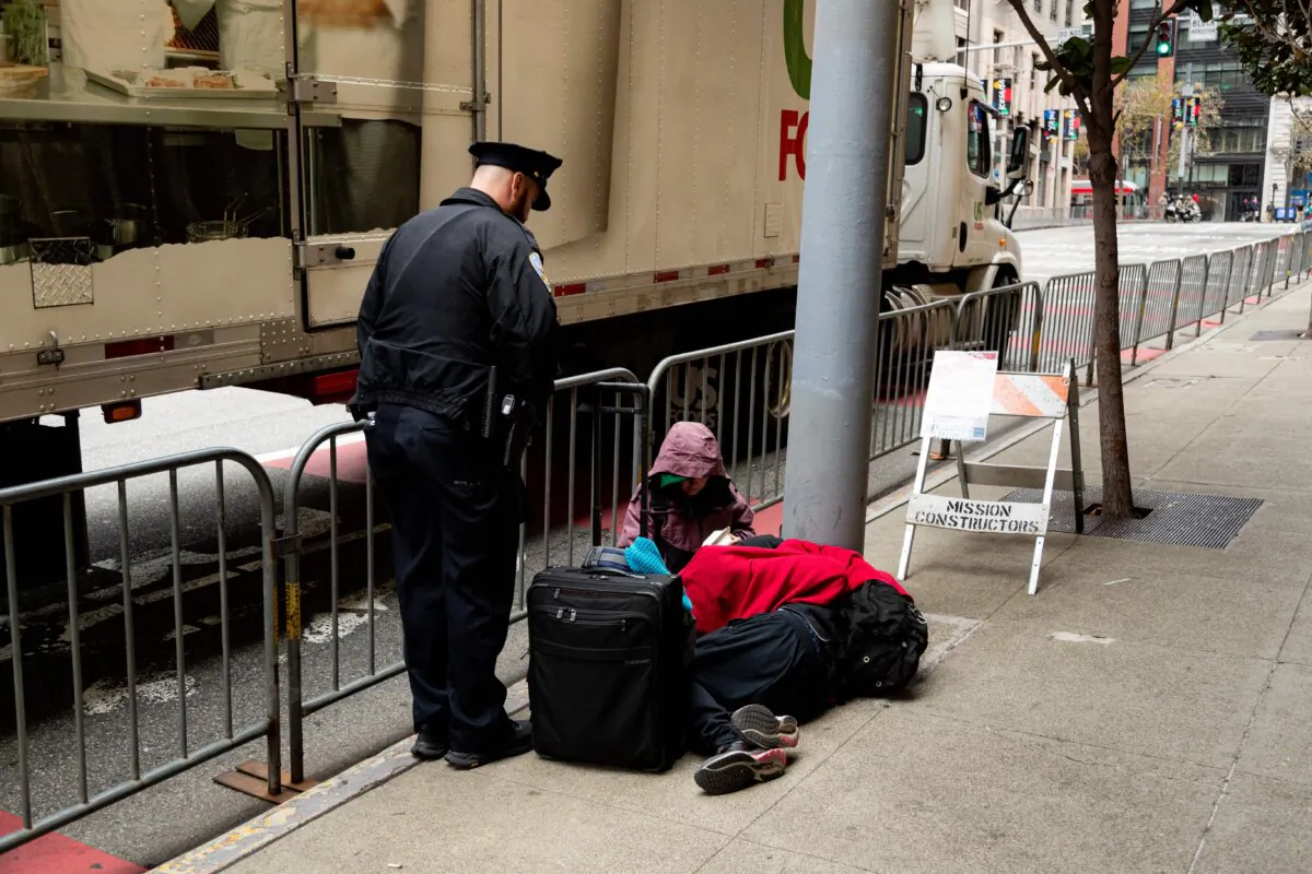 A San Francisco Police Department officer asks two people sitting on the sidewalk to move during the Asia-Pacific Economic Cooperation (APEC) leaders’ week in San Francisco on Nov. 14, 2023. (Jason Henry/AFP via Getty Images)