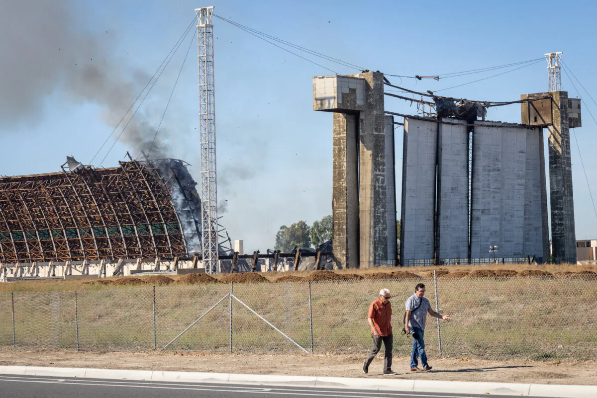 Men walk as a fire continues to burn a historic blimp hangar in Tustin, Calif., on Nov. 14, 2023. (John Fredricks/The Epoch Times)