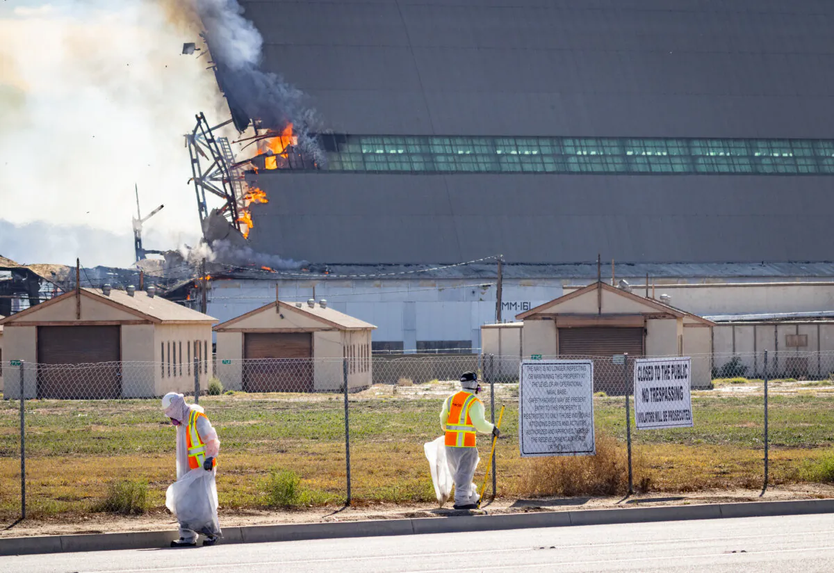 Men search for hazardous materials as a fire continues to burn a historic blimp hangar in Tustin, Calif., on Nov. 14, 2023. (John Fredricks/The Epoch Times)