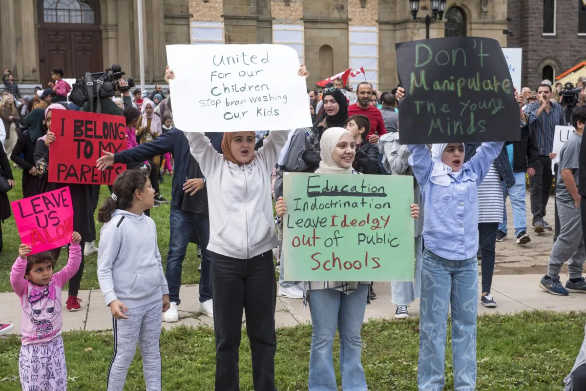 Protesters hold signs about gender ideology in schools, standing in front of the New Brunswick legislature in Fredericton on Sept. 20, 2023. (The Canadian Press/Stephen MacGillivray)