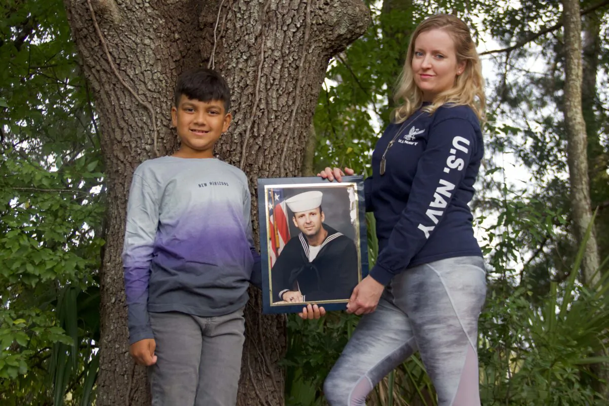 Luke Sukhram (left), 8, and his mother Sabrina Davis (right) stand with a photo of her father, Keith Davis, in Gainesville, Fla. on Nov. 1, 2021 after Mr. Davis passed away in 2020 due to medical negligence. (Courtesy Kiara Cline)