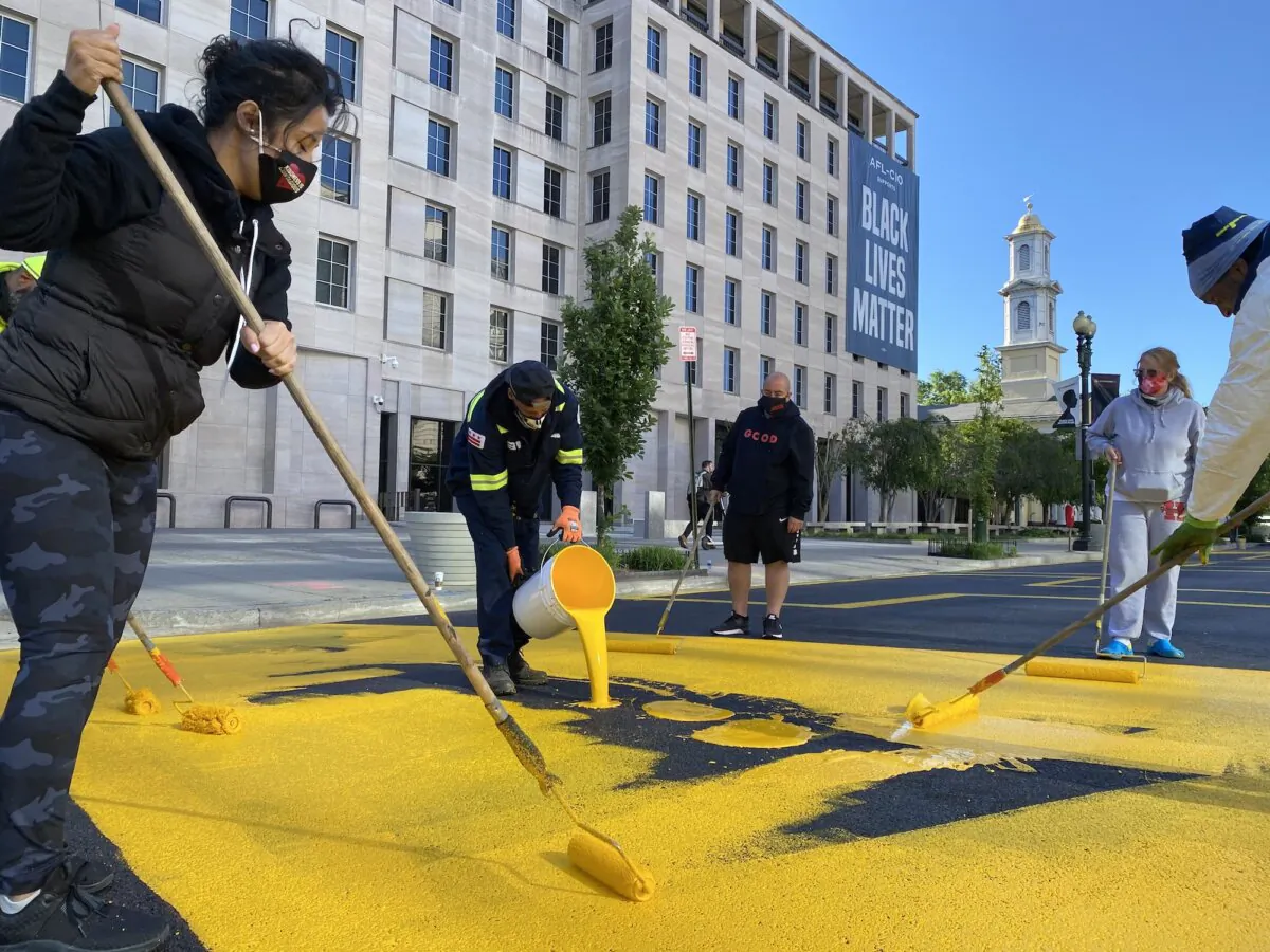 People add a coat of paint to the Black Lives Matter sign that runs two city blocks near the White House on what was part of 16th Street but was renamed Black Lives Matter Plaza in Washington, on May 13, 2021. (Eric Baradat/AFP/Getty Images)