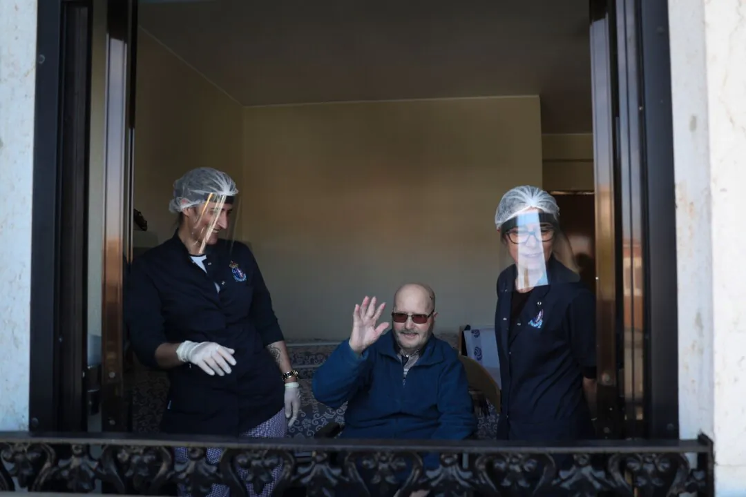 An elderly resident at Santo Antonio retirement house in Figueira da Foz, waves from his window to his relatives, who stand on a manlift crane to keep their social distance, in Portugal, on May 7, 2020. (Carlos Costa/AFP via Getty Images)