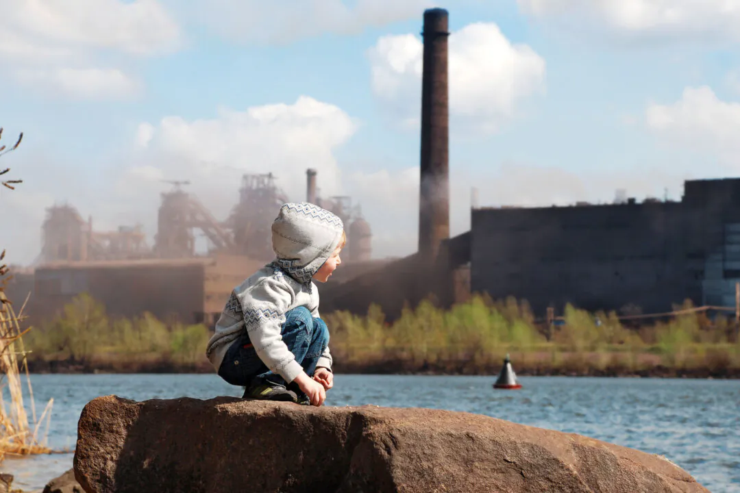 A little boy plays by the river across from a smokestack and the thick haze of polluted air. (Soloviova Liudmyla/Shutterstock)