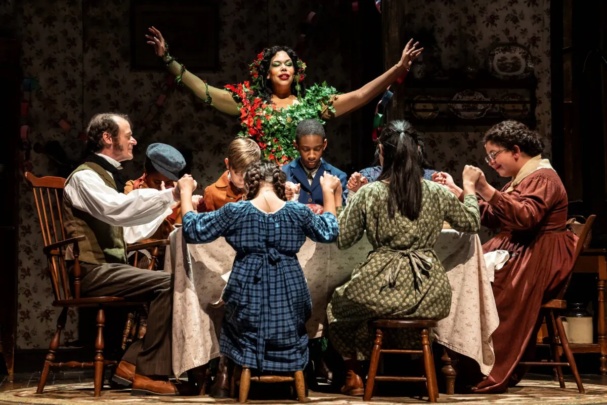 (Sitting L–R) The family of Bob Cratchits: Bob (Thomas J. Cox), Tiny Tim (Christian Lucas), Peter (Leighton Tantillo), Gregory (Amir Henderson), and Mrs. Cratchit (Susaan Jamshidi). (Standing) The Ghost of Christmas Present (Bethany Thomas), in “A Christmas Carol.” (Liz Lauren)