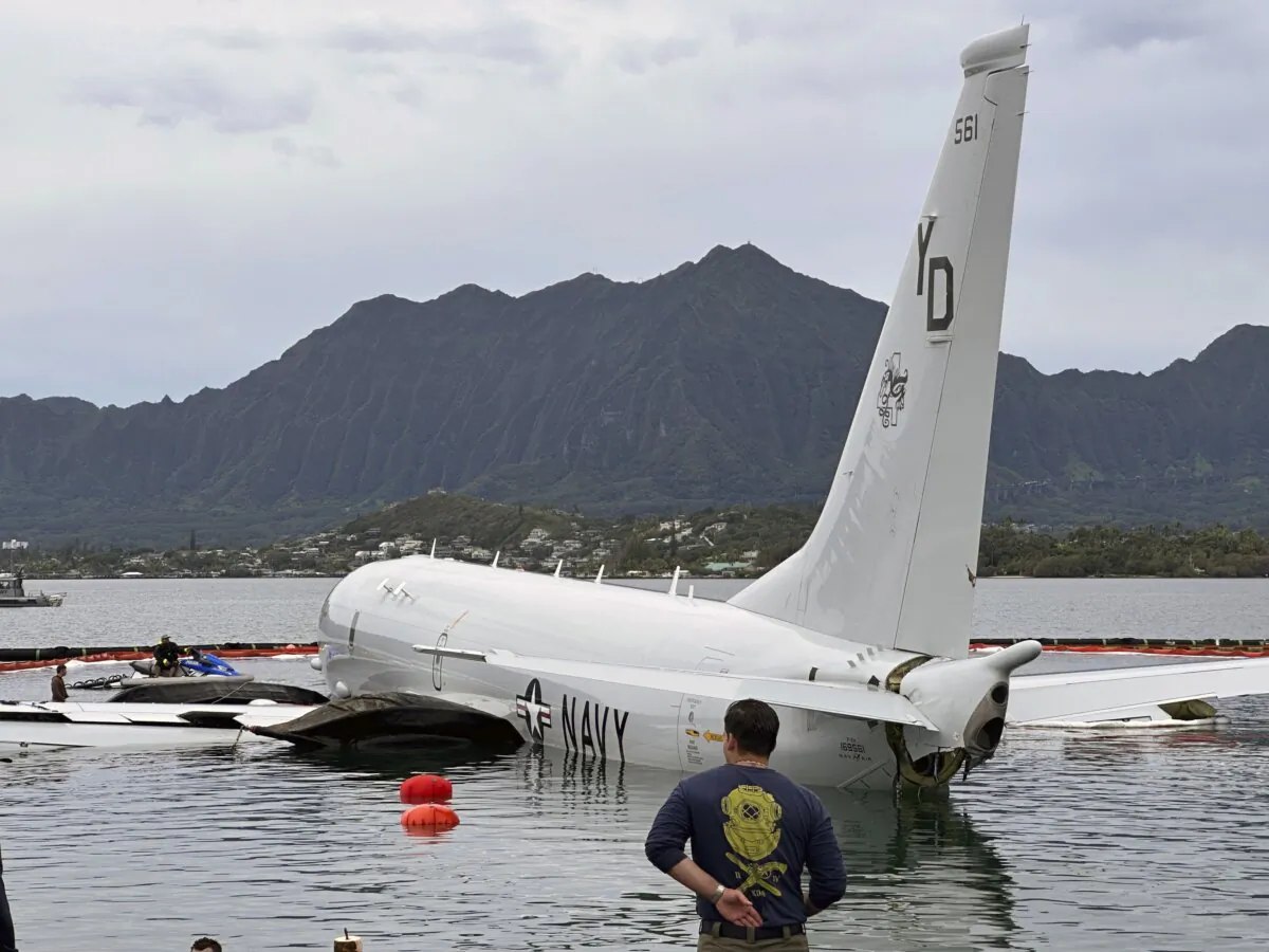 Contractors place inflatable bags under a U.S. Navy P-8A in Kaneohe Bay, Hawaii, on Dec. 1, 2023, so they can float the aircraft over the water and onto land. (Audrey McAvoy/AP Photo)