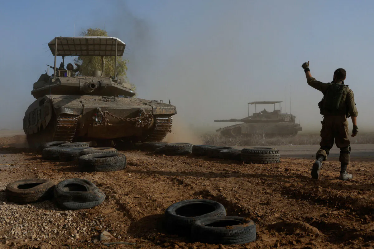 An Israeli soldier gestures towards a tank crew member as it crosses a road, as part of the convoy near Israel's border with southern Gaza, in Israel, on Dec. 4, 2023. (Amir Cohen/Reuters)