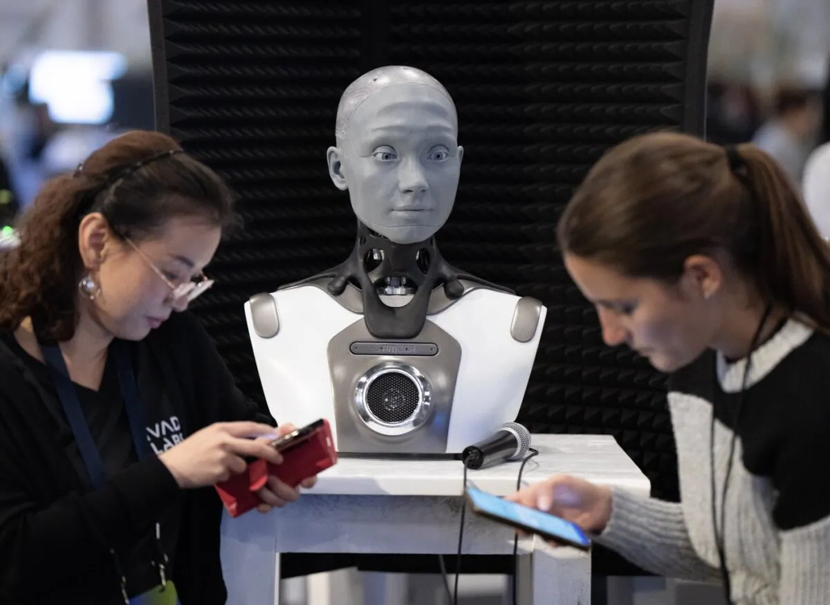 People check their phones as AMECA, an AI robot, looks on at the All In artificial intelligence conference in Montreal on Sept. 28, 2023. (Ryan Remiorz /The Canadian Press)