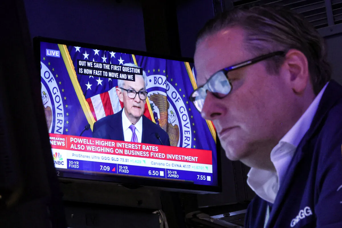 A trader works, as a screen displays a news conference by Federal Reserve Board Chairman Jerome Powell following the Fed rate announcement, on the floor of the New York Stock Exchange (NYSE) in New York City on Dec. 13, 2023. (Brendan McDermid/Reuters)