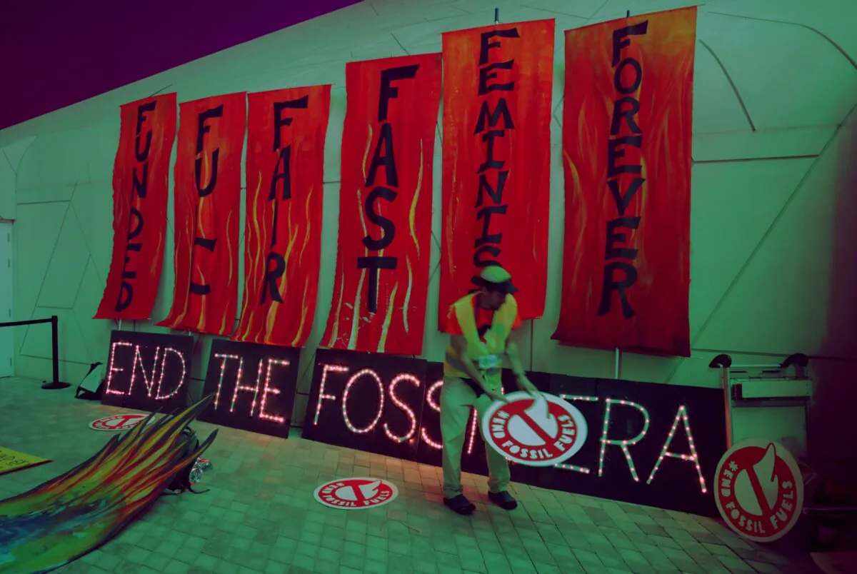 An activist places protest signs on the ground next to an illuminated sign that reads: "End the fossil era" following a protest to demand a phase out of fossil fuels on day twelve at the UNFCCC COP28 Climate Conference in Dubai, United Arab Emirates, on Dec. 12, 2023. (Sean Gallup/Getty Images)