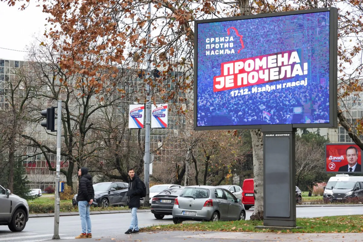 People stand next to a pre-election billboard of the opposition coalition 'Serbia Against Violence' in Belgrade, Serbia, on Dec. 14, 2023. (Zorana Jevtic/Reuters)