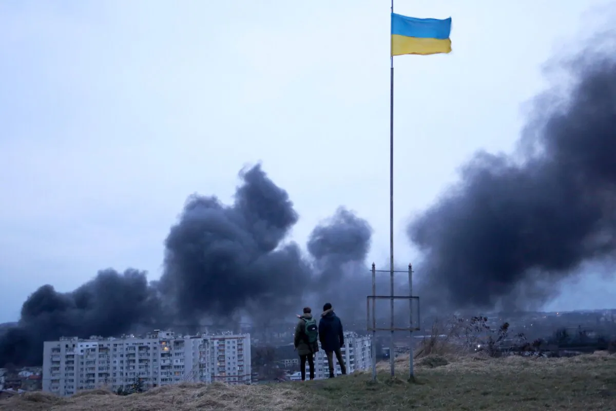 People standing near a Ukrainian national flag watch as dark smoke billows following an air strike in the western Ukrainian city of Lviv, on March 26, 2022. (Oleksii Filippov/AFP via Getty Images)