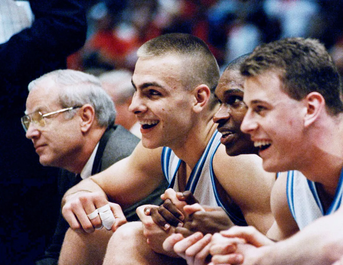 (L–R) North Carolina's Eric Montross, Donald Williams and Pat Sullivan smile as they hold hands and sit out the last seconds of their overtime victory against Cincinnati at the NCAA East Regional Final in the Meadowlands Arena on March 28, 1993 in East Rutherford, N.J. Montross, the former North Carolina and NBA big man, has died after a cancer fight, his family said. (Charles Rex Arbogast/AP Photo)