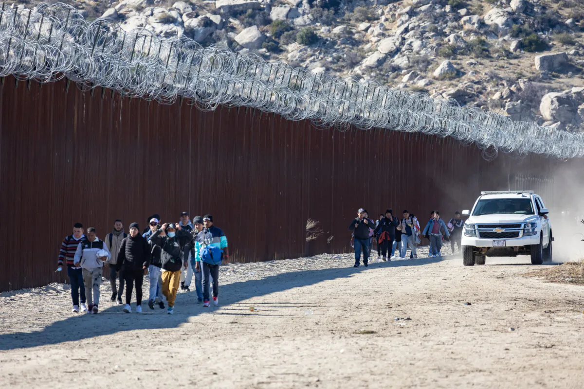 Illegal immigrants who passed through a gap in the U.S. border wall await processing by Border Patrol agents in Jacumba, Calif., on Dec. 7, 2023. (John Fredricks/The Epoch Times)