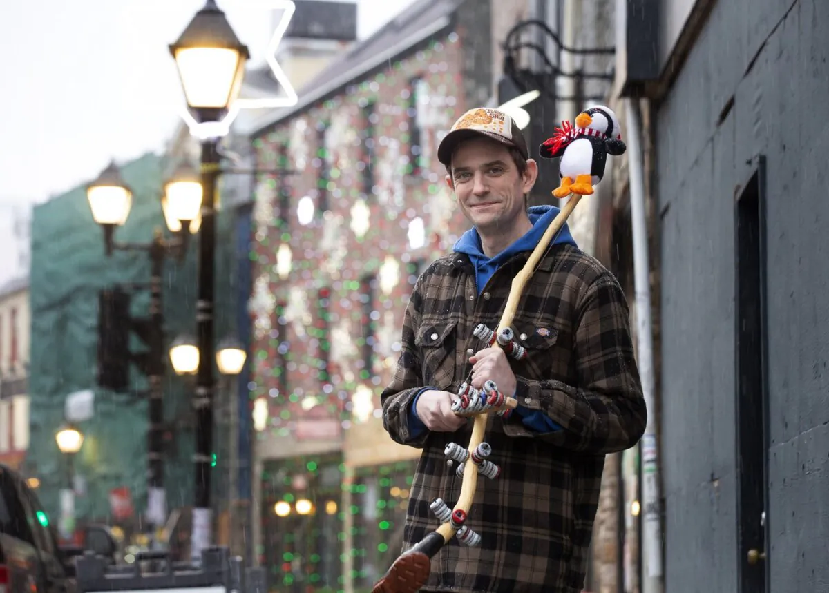 Dave Rowe, owner of O'Brien's Music Store poses with an ugly stick: a traditional Newfoundland and Labrador percussion musical instrument, outside his shop on Water Street, St. John's, on Dec. 4, 2023. (The Canadian Press/Paul Daly)