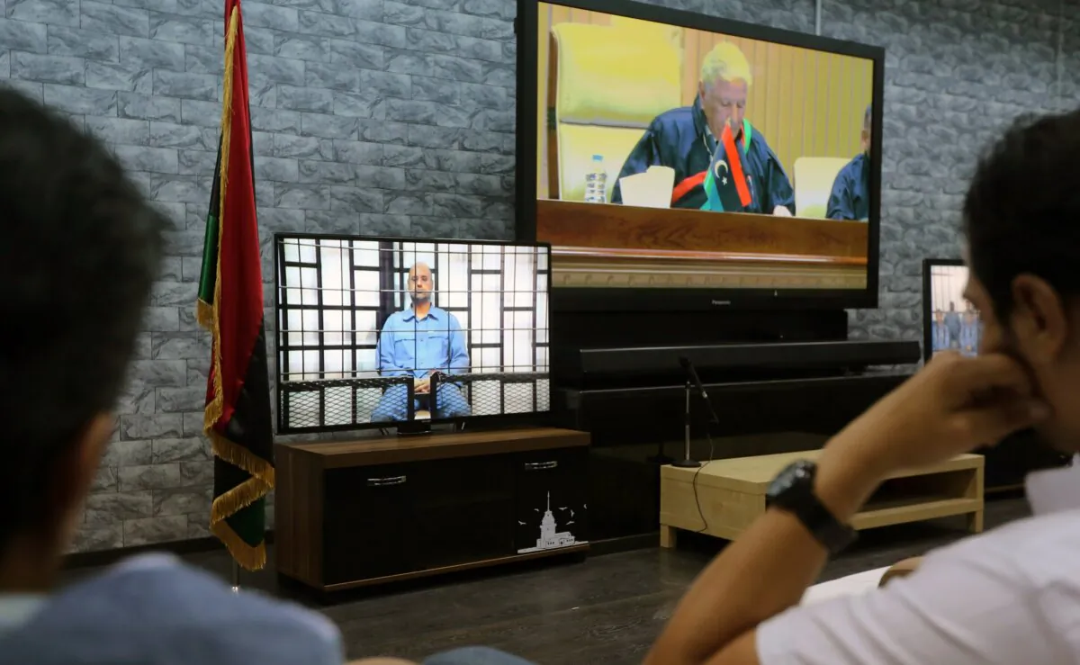 Journalists watch TV screens showing a judge (R), broadcasted live from an adjacent room, questionning Seif al-Islam (L), the son of slain Libyan dictator Muammar Gaddafi, broadcasted from the western Libyan city of Zintan during his trial in a courthouse in Tripoli on May 25, 2014. (Mahmud Turkia/AFP via Getty Images)