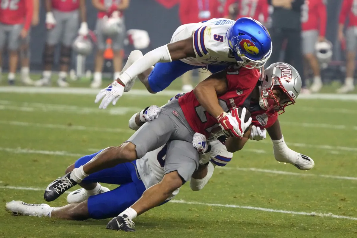 UNLV wide receiver Jacob De Jesus is tackled by Kansas safety O.J. Burroughs (5) and linebacker Taiwan Berryhill Jr. during the first half of the Guaranteed Rate Bowl NCAA college football game in Phoenix on Dec. 26, 2023. (Rick Scuteri/AP Photo)