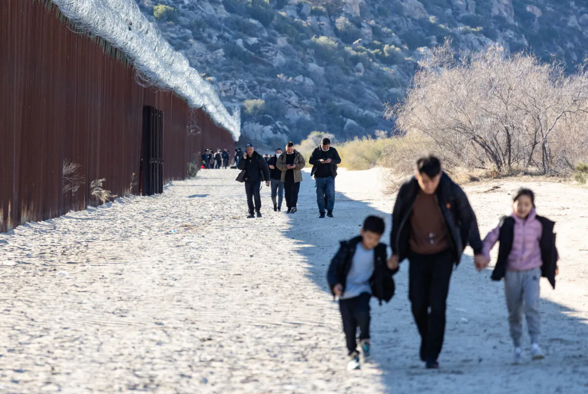 Migrants walk along the U.S. side of the United States border wall after crossing through a gap in Jacumba, Calif., on Dec. 6, 2023. (John Fredricks/The Epoch Times)