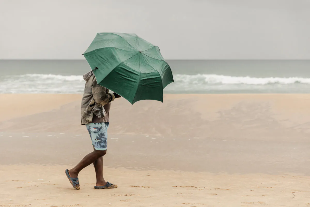A local holidaymaker uses an umbrella to protect himself against the rain and braves the inclement weather at the South beach during Boxing Day festivities in Durban, on Dec. 26, 2023. (Rajesh Jantilal/AFP via Getty Images)