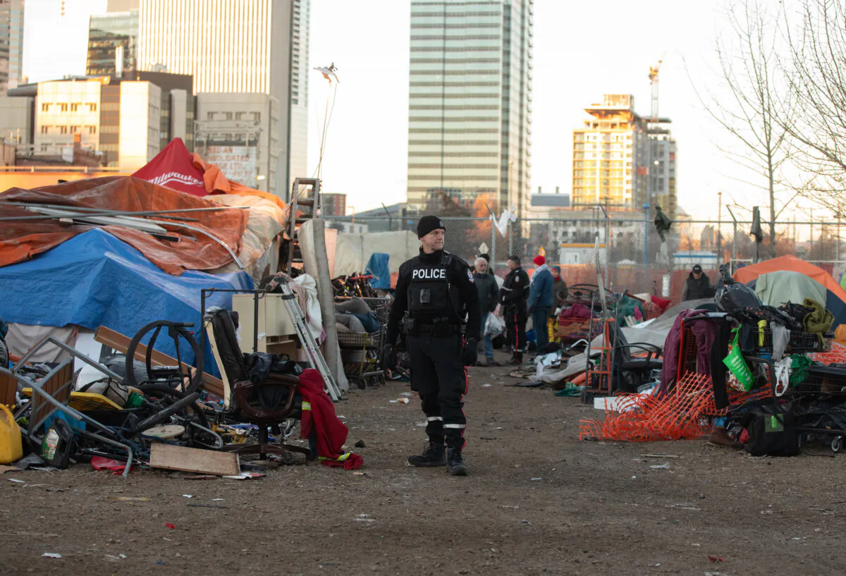 A police officer keeps an eye on things as police and cleanup crews tear down homeless encampments in Edmonton on Dec. 29, 2023. (THE CANADIAN PRESS/Jason Franson)