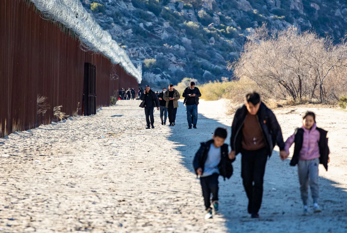 Migrants walk along the US side of the United States border wall after crossing through an open gap in Jacumba, Calif., on Dec. 6, 2023. (John Fredricks/The Epoch Times)