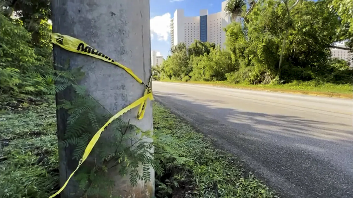 Police tape is wrapped around a pole with Tsubaki Towers in the background in Tamuning, Guam, on Jan. 5, 2024, after a fatal shooting on Jan. 4. (KUAM-TV via AP)