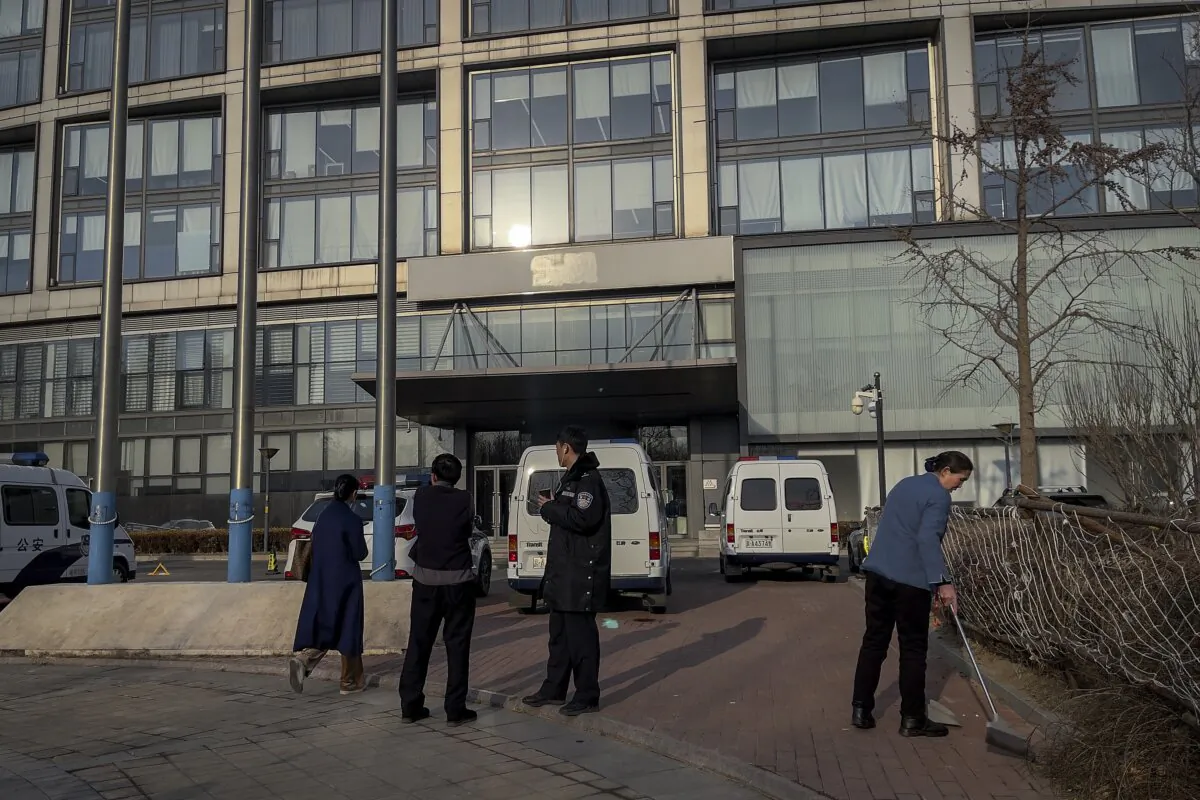 A police officer talks with a man near police vehicles parked outside the headquarters of the Zhongzhi Enterprise Group Co. in Beijing on Jan. 8, 2024. (Andy Wong/AP Photo)