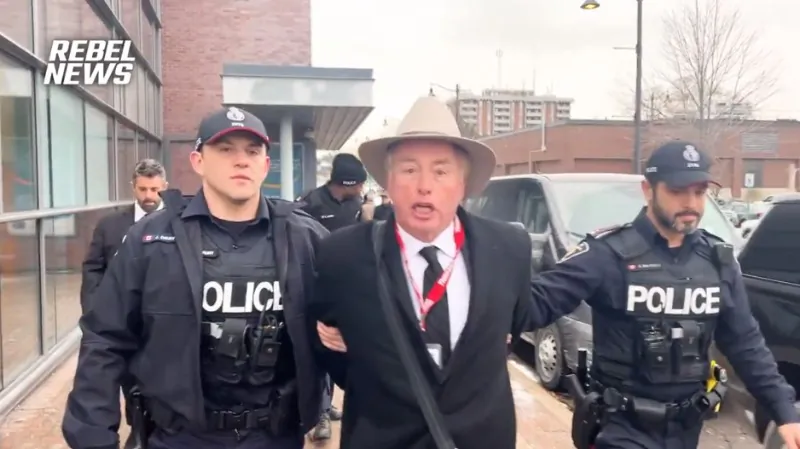 Rebel News reporter David Menzies is handcuffed by York Regional Police officers and taken to a police car in Richmond Hill, Ont., on Jan. 8, 2024. (Screenshot/Rebel News Video)