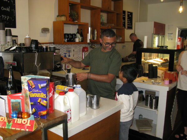 Zee Lalani, former owner of Charlie and Leo's Cafe in Melbourne, Australia speaks to his son while making coffee on Dec. 24, 2023. (Henry Jom/The Epoch Times)