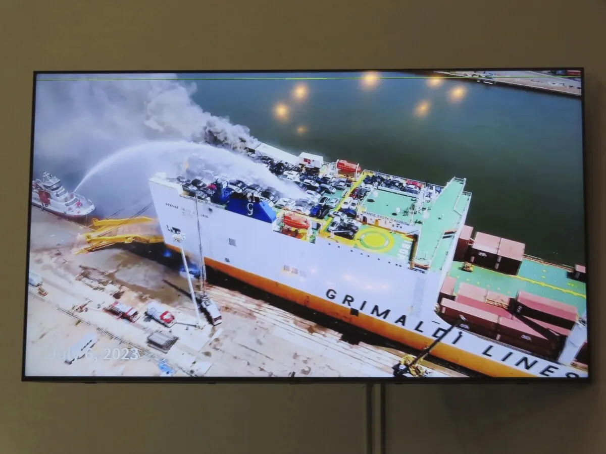 A photo displayed on a video monitor in Union, N.J., Wednesday, Jan. 10, 2024 shows a burning cargo ship in Newark N.J. on July 5, 2023. Federal investigators are conducting hearings into the blaze that killed two Newark, N.J. fire captains. (AP Photo/Wayne Parry)
