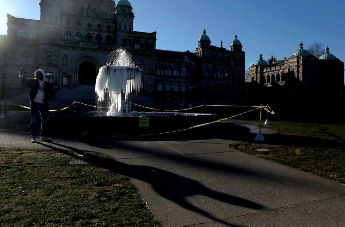 Cold temperatures across the province set in as a man takes a picture of the fountain out front of the legislature freezing over during a cold spell in Victoria, B.C., on Jan.12, 2024. (The Canadian Press/Chad Hipolito)