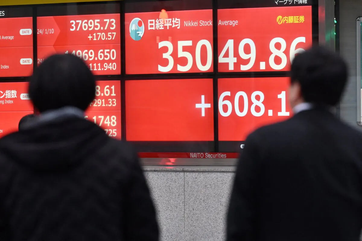 Pedestrians walk past a signboard showing the closing numbers on the Tokyo Stock Exchange, along a street in Tokyo in Jan. 11, 2024. (Richard A. Brooks / AFP via Getty Images)