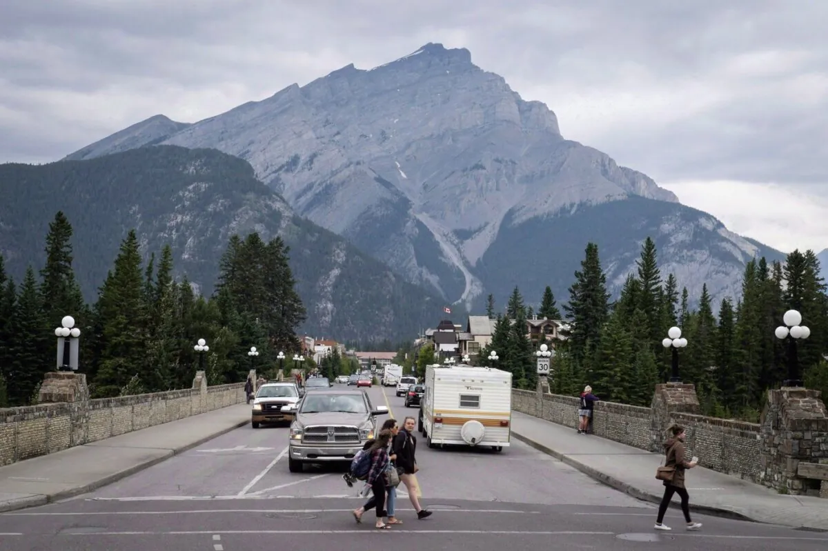 People walk across a street in Banff, Alta., in Banff National Park, on July 21, 2017. (The Canadian Press/Jeff McIntosh)