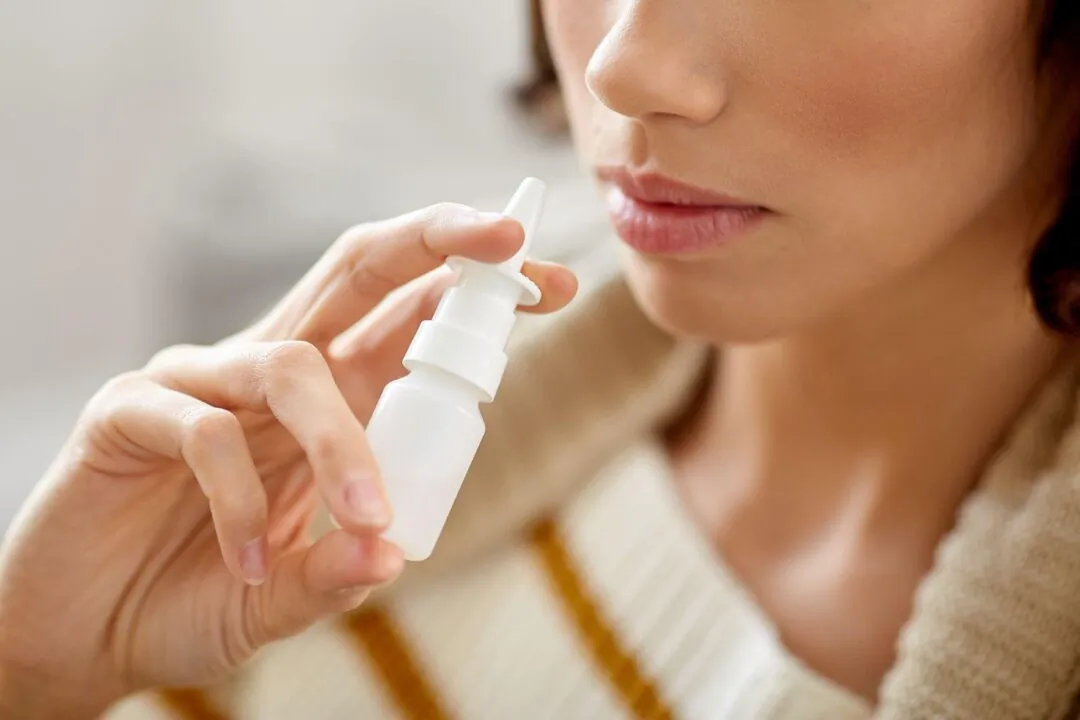 A woman holds a nasal spray bottle. (Ground Picture/Shutterstock)