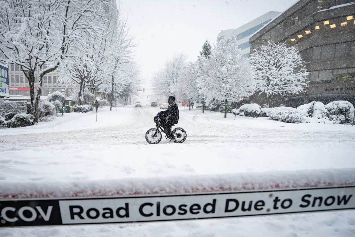 A person cycles past a road closed sign during a snowstorm in Vancouver on Jan. 17, 2024. (The Canadian Press/Ethan Cairns)