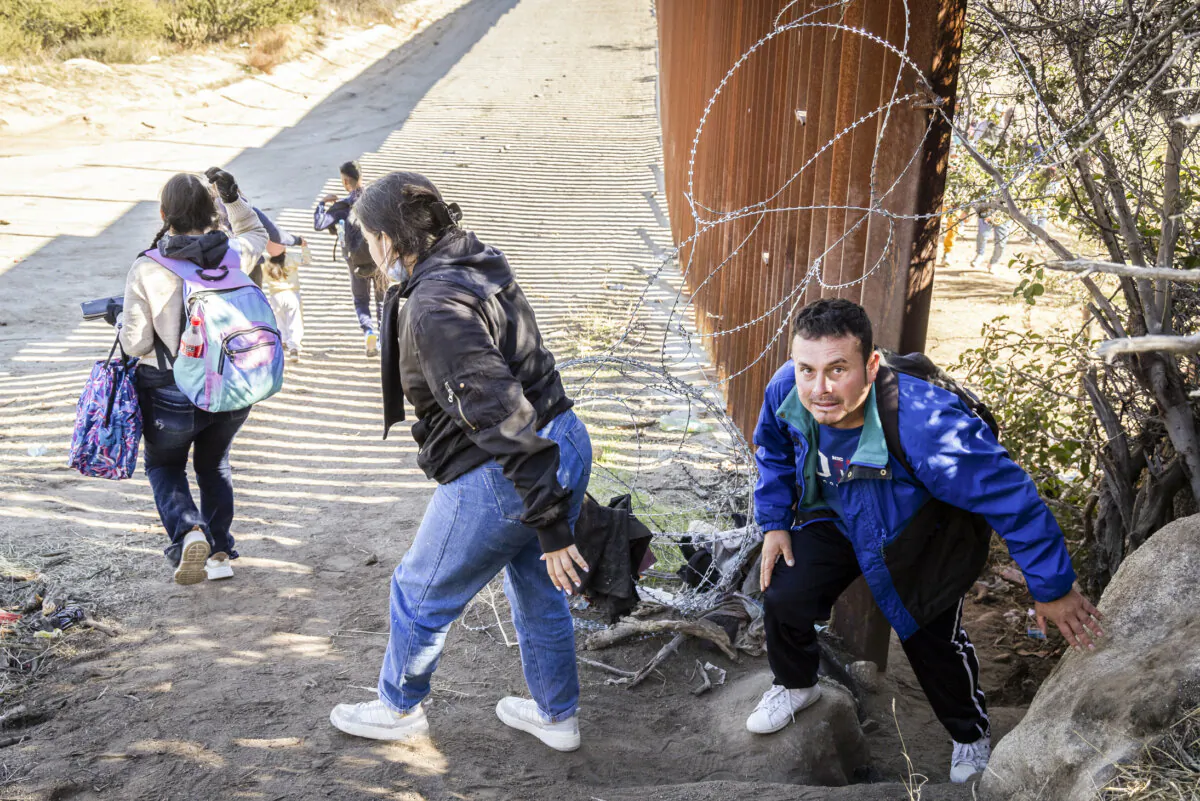 Illegal immigrants pass through a gap in the United States border wall to await processing by Border Patrol agents in Jacumba, Calif., on Dec. 7, 2023. (John Fredricks/The Epoch Times)
