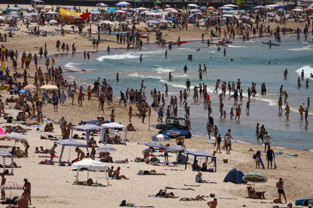 Beachgoers sit and stand on the sand as others swim on a hot summer day at Sydney's Bondi Beach on Dec. 9, 2023. (DAVID GRAY/AFP via Getty Images)