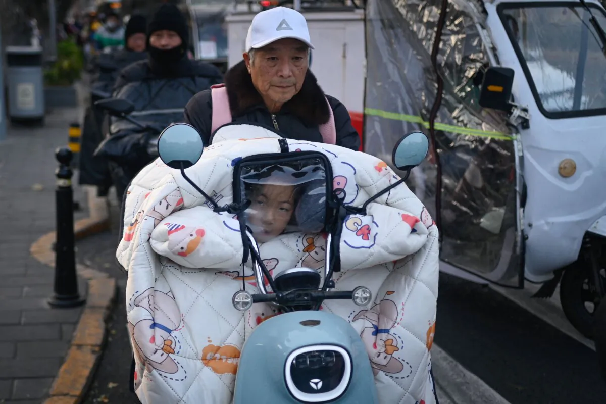 A child peers through the visor of a windbreaker on an electric scooter while returning from school in Beijing on November 22, 2023. (Wang Zhao / AFP via Getty Images)