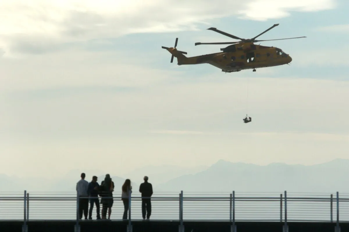 People look on as the AgustaWestland CH-149 Cormorant helicopter demonstrates a search and rescue operation during the Defence on the Dock at the Ogden Point Breakwater District in Victoria, on Sept. 17, 2023. (The Canadian Press/Chad Hipolito)