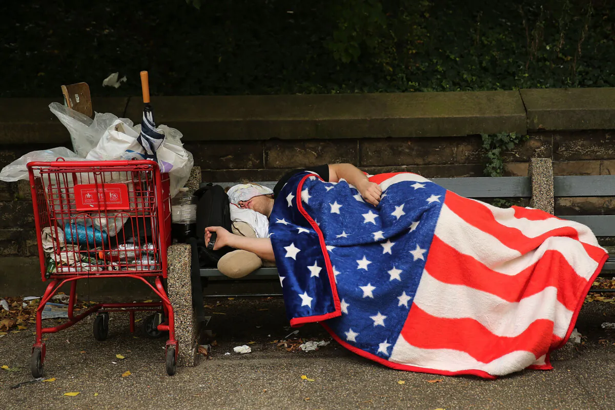 A homeless man sleeps under an American Flag blanket on a park bench in the Brooklyn borough of New York City on Sept. 10, 2013. (Spencer Platt/Getty Images)