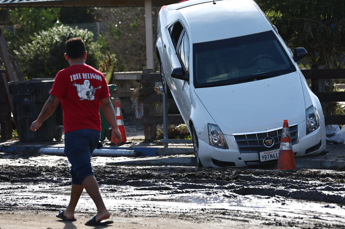 A person stands near a vehicle moved by flooding that remains lodged on a fence the day after an explosive rainstorm deluged areas of San Diego County in San Diego on Jan. 23, 2024. (Mario Tama/Getty Images)
