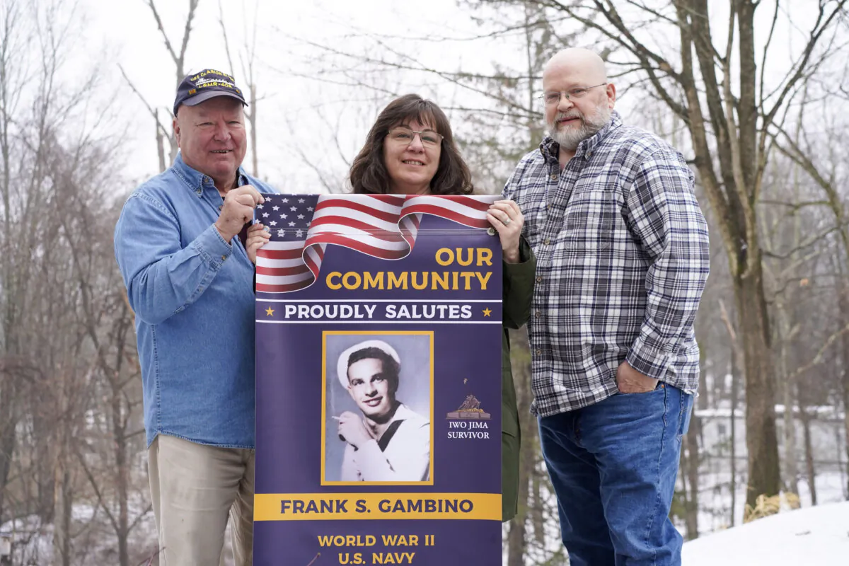 Phil Adamson (L), Heidi Phillips (C), and Mike Phillips (R) hold up a veteran banner honoring Mr. Adamson's father-in-law, Frank Gambino, in Otisville, N.Y., on Jan. 24, 2024. (Cara Ding/The Epoch Times)