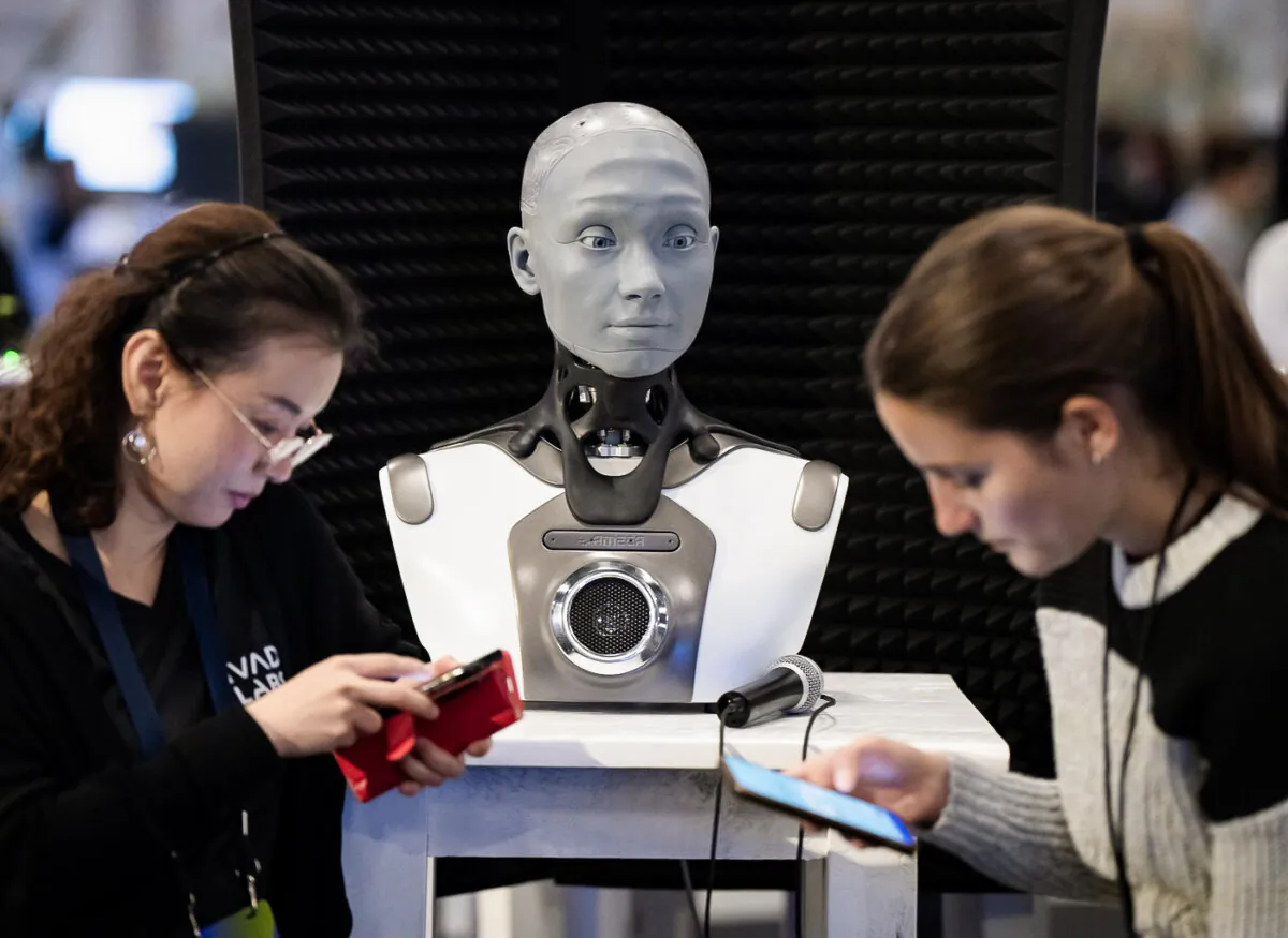 People check their phones as AMECA, an AI robot, looks on at the All In artificial intelligence conference in Montreal on Sept. 28, 2023. (Ryan Remiorz /The Canadian Press)