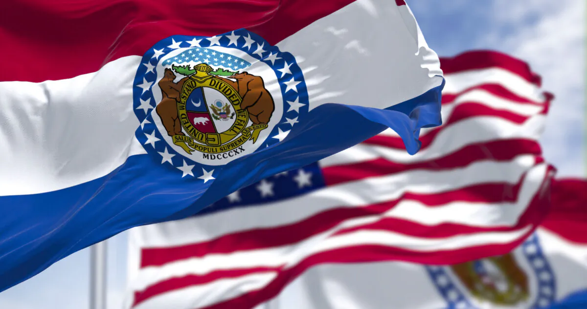 The Missouri state flag waving along with the national flag of the United States of America. In the background there is a clear sky. Missouri is a state in the Midwestern region of the United States