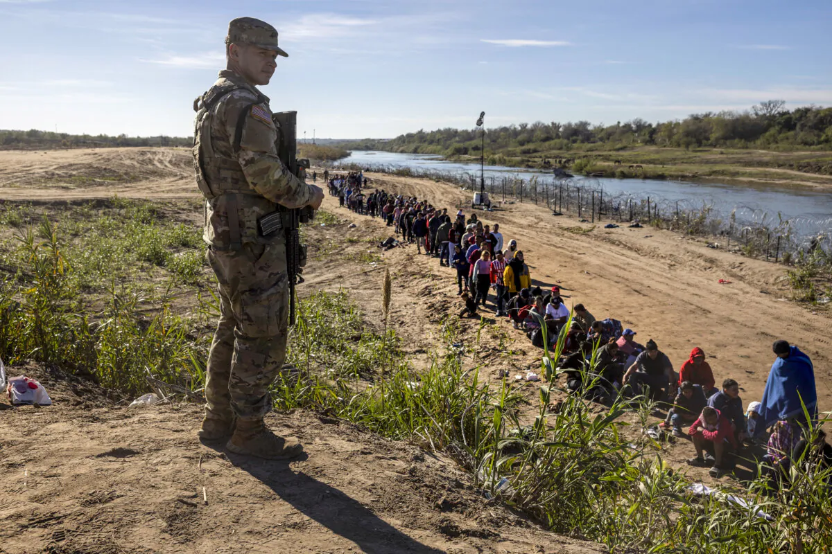 A Texas National Guard soldier watches over a group of more than 1,000 migrants who had crossed the Rio Grande from Mexico in Eagle Pass, Texas, on Dec. 18, 2023. (John Moore/Getty Images)
